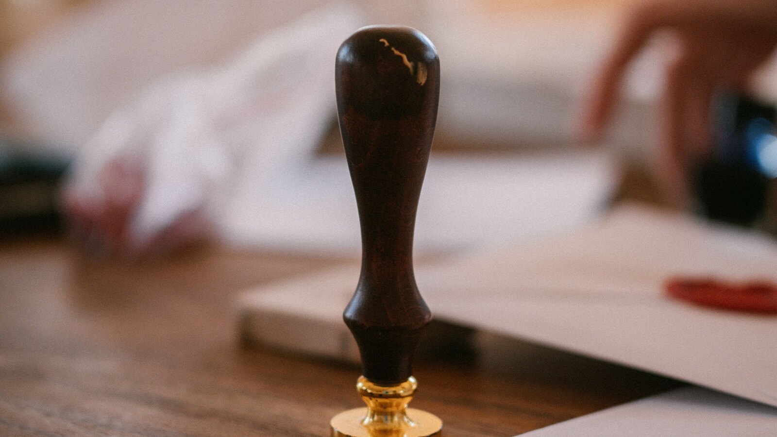 A notary wax seal stamp resting on a desk beside sealed papers